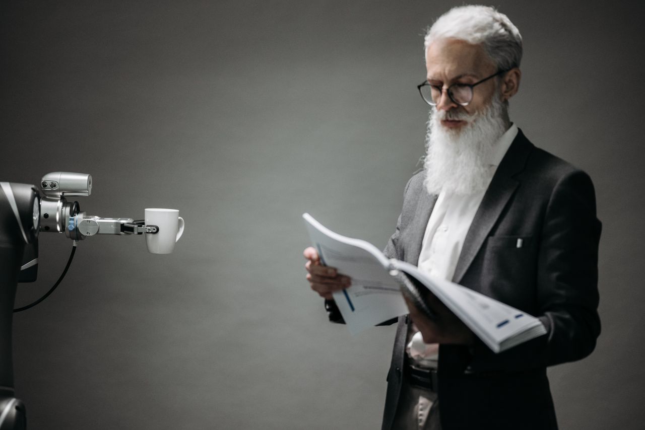 A robot arm assists a professional with a book and coffee in a modern office setup. Technology meets innovation.